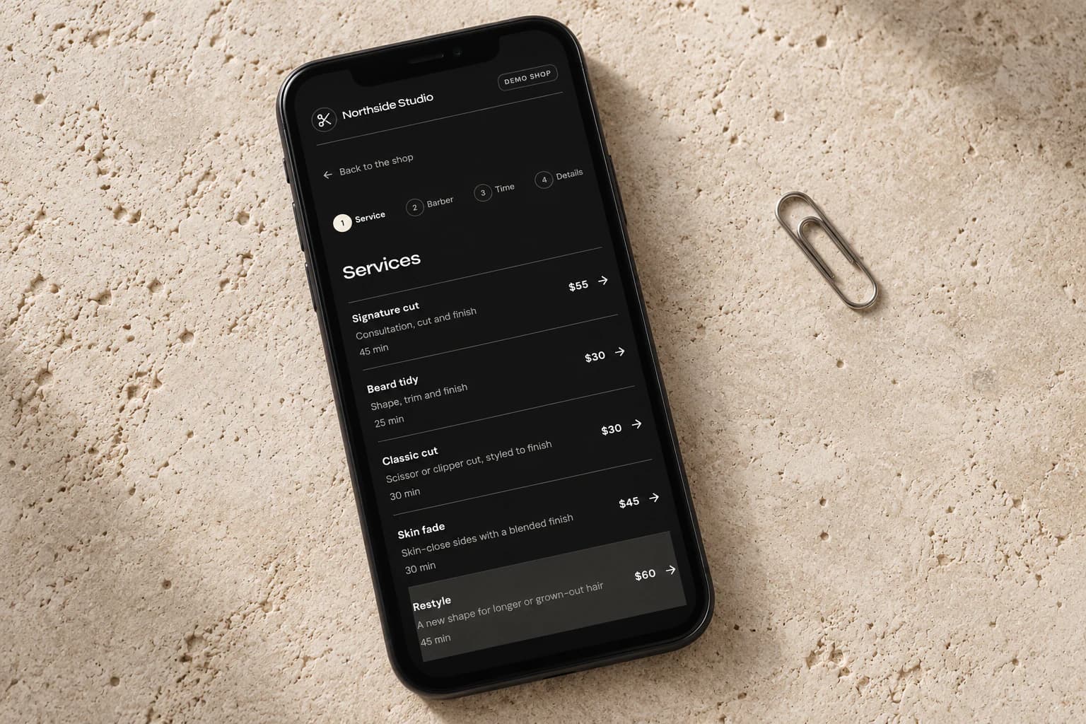 Phone displaying the CalendarCut demo booking page in dark mode on pale stone