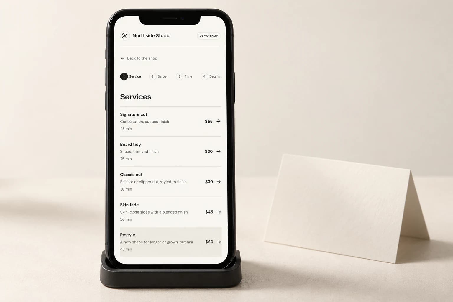 Phone displaying the CalendarCut demo shop's service booking page on an ivory tabletop
